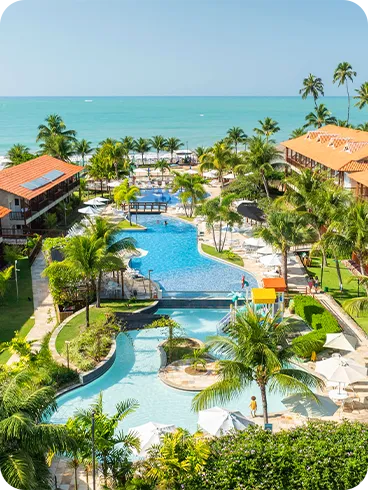 Resort Salinas Maceió Vista aérea do Salinas Maceió com prédios de telhados laranja, piscinas sinuosas e o mar azul ao fundo em dia ensolarado.