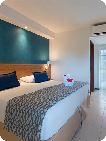 acomodação standard Cama queen size na acomodação Standard, decorada com ursinho  feito de toalha, em frente a roupeiro e painel de madeira com TV a cabo, mesa e cadeira.