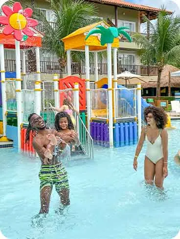Resort pra família Família brincando no parque aquático infantil do Salinas Maceió, com toboágua verde, jatos d’água e piscina rasa.