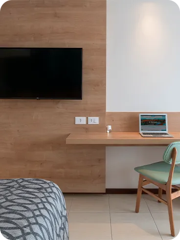 interior da acomodação superior Painel de madeira que fica em frente às camas, com TV a cabo, mesa, cadeira e espelho ao lado.