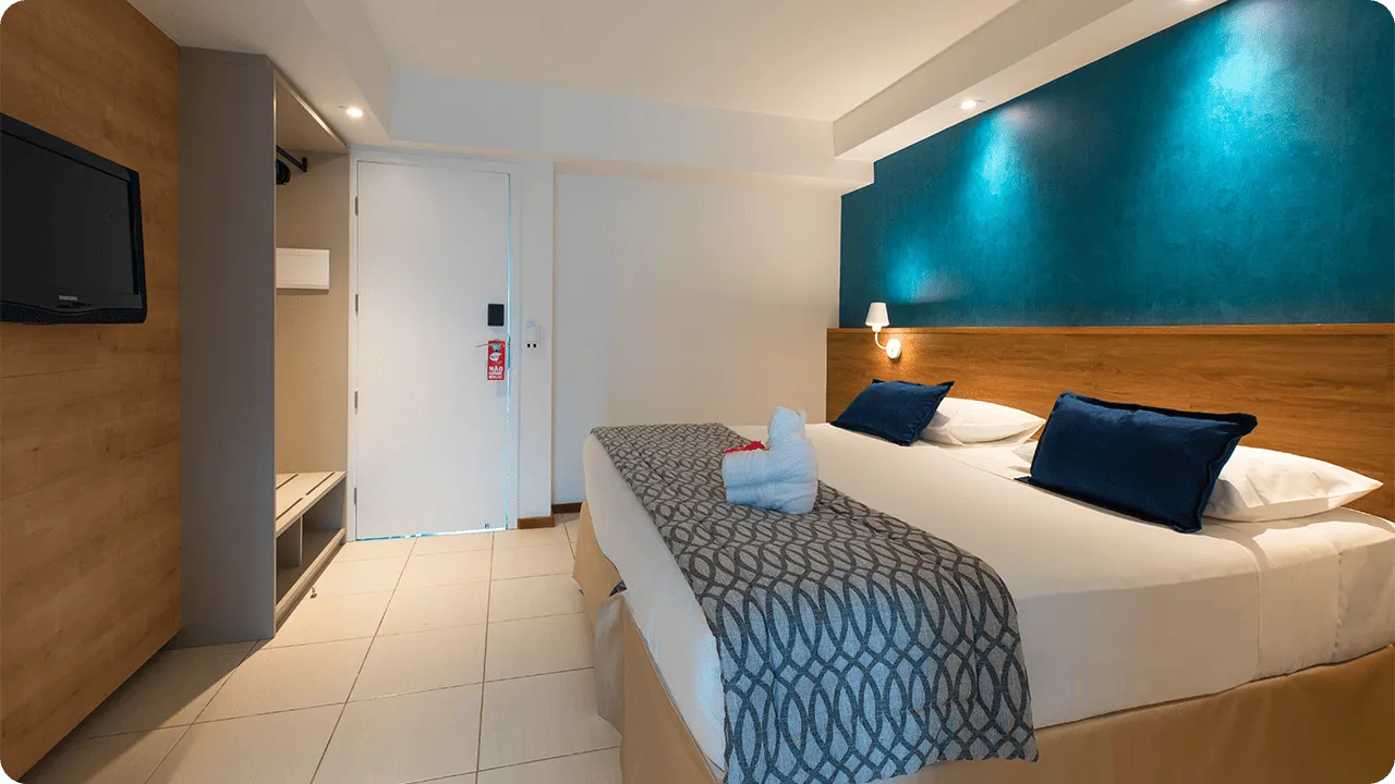 apartamento standard Cama queen size na acomodação Standard, em frente a roupeiro e painel de madeira com TV a cabo, mesa e cadeira.