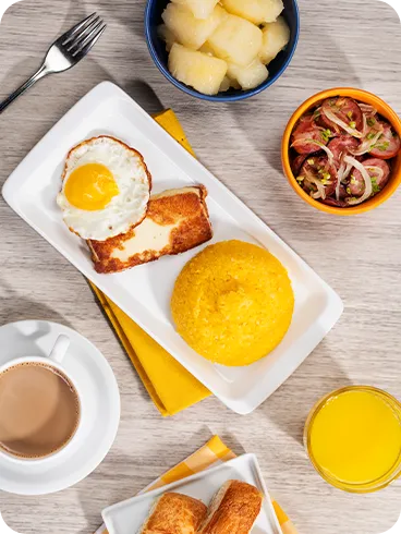 Café da manhã all inclusive Prato com cuscuz amarelo, ovo frito e queijo coalho; ao lado, macaxeira cozida, linguiça acebolada, folhados, suco de laranja e café com leite — café da manhã do Salinas Maragogi all inclusive.