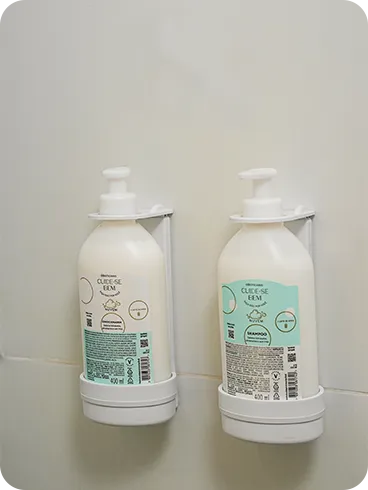 Dispensers de Refil O Boticário Shampoo e condicionador O Boticário, da linha Cuide-se Bem, em frascos de refil instalados em dispensers na parede de azulejos do banheiro.
