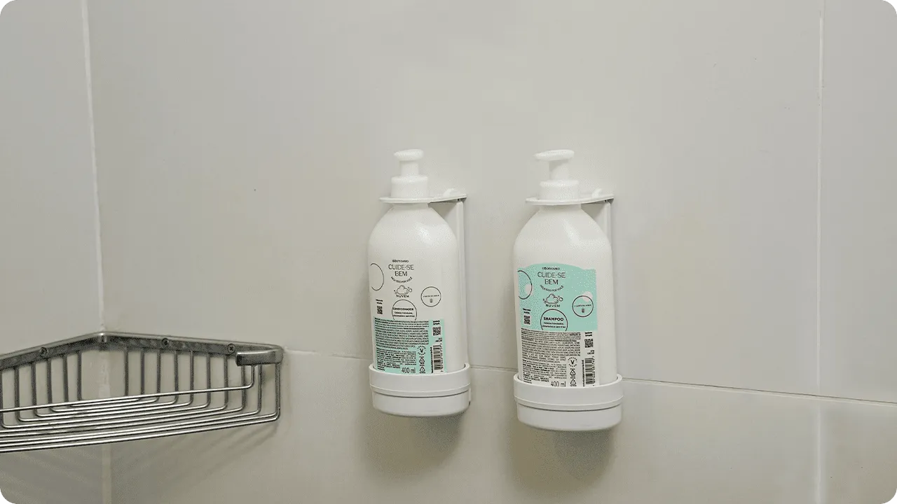 Dispensers de Refil O Boticário Shampoo e condicionador O Boticário, da linha Cuide-se Bem, em frascos de refil instalados em dispensers na parede de azulejos do banheiro.