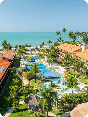 Resort completo à beira-mar em Maceió Visão aérea do Salinas Maceió com piscinas sinuosas, blocos de apartamentos, muitos coqueiros e o mar ao fundo.