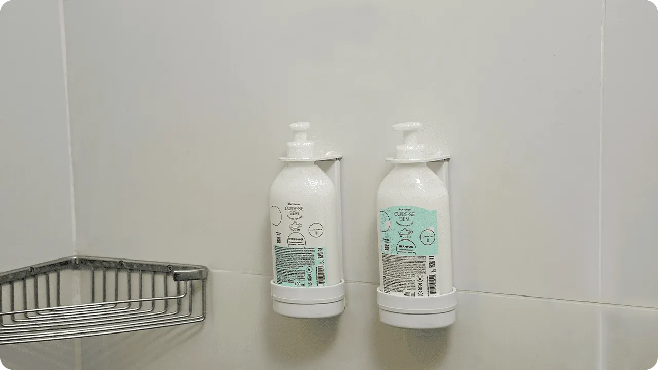 Dispensers de Refil O Boticário Shampoo e condicionador O Boticário, da linha Cuide-se Bem, em frascos de refil instalados em dispensers na parede de azulejos do banheiro.