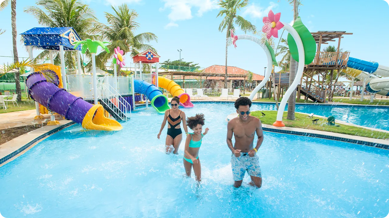Parque Acuático Salinas Maragogi Una familia sonriente corre y juega en la piscina infantil del parque acuático, que cuenta con varios toboganes y coloridas atracciones. Padre, madre e hija disfrutan de un día soleado en el resort.