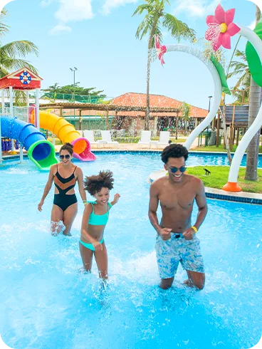 Parque Acuático Salinas Maragogi Una familia sonriente corre y juega en la piscina infantil del parque acuático, que cuenta con varios toboganes y coloridas atracciones. Padre, madre e hija disfrutan de un día soleado en el resort.