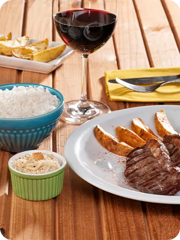All Inclusive de verdade Prato de bacalhau e pedaços de carne assada acompanhadas de batatas rústicas, arroz e vinhos.
