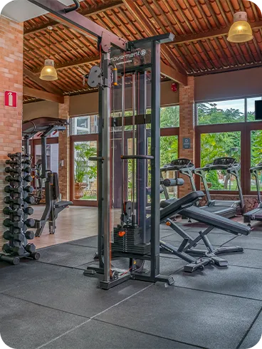 Resort com academia Academia ampla do resort com piso emborrachado, máquinas de musculação, racks de halteres e esteiras voltadas para janelas com vista para o jardim.