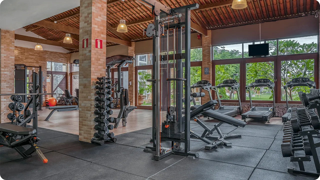 Resort com academia Academia ampla do resort com piso emborrachado, máquinas de musculação, racks de halteres e esteiras voltadas para janelas com vista para o jardim.