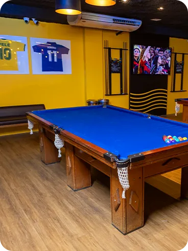 Bar no salinas maceió Salão do bar com duas mesas de sinuca de pano azul, paredes amarelas, camisas de futebol emolduradas, TV transmitindo jogo, bancos altos e piso de madeira.