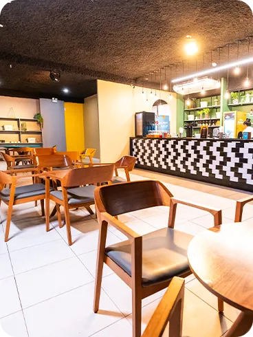 Resort all inclusive Lounge de bar amplo com balcão estampado em preto e branco, prateleiras verdes com garrafas, luminárias pendentes, mesas redondas de madeira e cadeiras estofadas; ambiente claro e aconchegante para curtir bebidas e petiscos.