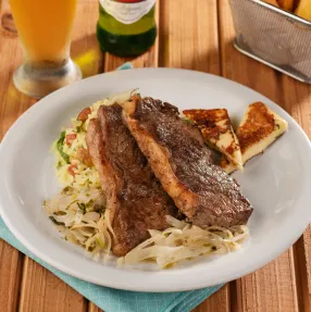 Carne com massa e queijo coalho no Salinas Maceió Prato de jantar com carne fatiada sobre massa e risoto, acompanhado de queijo coalho grelhado. A refeição é servida com batata frita e uma cerveja Stella Artois gelada.