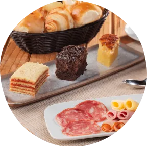 Melhor café da manhã no resort na praia Café da manhã completo com cesta de pães, frios, bolos variados, salada de frutas e café preto sobre a mesa.