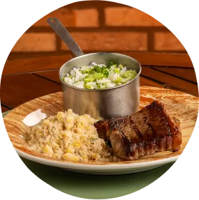 Almoço com sabor caseiro, frescor tropical no resort All inclusive Prato com arroz, carne grelhada e salada fresca sobre mesa de madeira com fundo de tijolos e talheres ao lado.