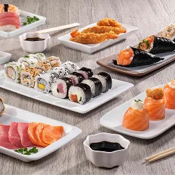 Sushi all inclusive Mesa repleta de sushis: rolinhos variados, niguiris, temakis, sashimis, hot rolls e potes de shoyu com hashis sobre tampo de madeira.