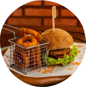 Hambúrguer artesanal e onion rings são o combo da noite perfeita no resort na praia Jantar com hambúrguer artesanal, onion rings crocantes e apresentação rústica sobre mesa de madeira.