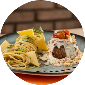 Jantar sofisticado com clima tropical e vista relaxante pra praia Jantar com espaguete ao molho de ervas, carne ao molho cremoso com tomatinhos assados e vinho tinto sobre uma mesa.