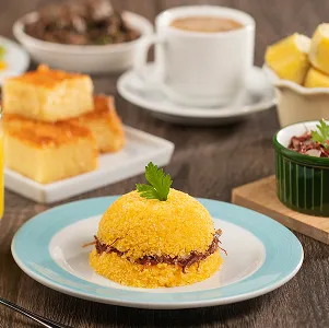 Café da manhã regional Mesa com cuscuz recheado de carne seca, suco de laranja, café, bolo de milho, frutas e acompanhamentos típicos do nordeste.