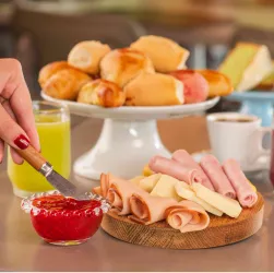 Café da manhã completo Mesa com pães, frios, queijos, geleia, café e sucos variados servidos no café da manhã.