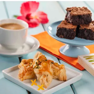 All Inclusive com doces e café Mesa com xícara de café, brownies de chocolate, folhados salgados e um livro ao fundo