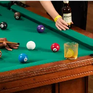 Diversão e drinks no All Inclusive Mesa de sinuca com bolas coloridas, copo com drink de limão e pessoa segurando cerveja Bohemia