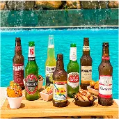 All inclusive completo Bandeja à beira da piscina com diversas cervejas geladas, Brahma, Beck’s, Corona, Original, Stella Artois, Bohemia e Budweiser, acompanhadas de petiscos, com cascata de pedras ao fundo.