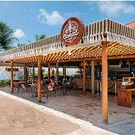 All inclusive pé na areia Bar de praia com cobertura de palha, mesas e cadeiras na areia, quiosques e vista direta para o mar.