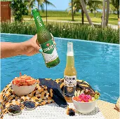 All inclusive completo Bandeja à beira da piscina com diversas cervejas geladas, Brahma, Beck’s, Corona, Original, Stella Artois, Bohemia e Budweiser, acompanhadas de petiscos, com cascata de pedras ao fundo.