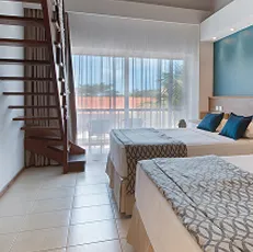 Apartamento Superior do Salinas Maceió Vista do quarto Apartamento Superior no Salinas Maceió, equipado com duas camas de casal, decoração moderna com parede azul, bancada de trabalho, TV e ar-condicionado.