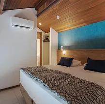 Apartamento com vista para o mar Quarto do resort com cama arrumada e porta da varanda aberta, revelando a vista para o mar azul e os coqueiros do Salinas Maceió.