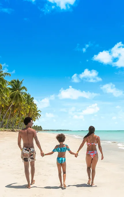 promoções salinas maragogi Família de costas caminhando sobre a areia branca à beira-mar da Praia de Xaréu, um dos destinos próximos ao Salinas Maragogi, em dia ensolarado.