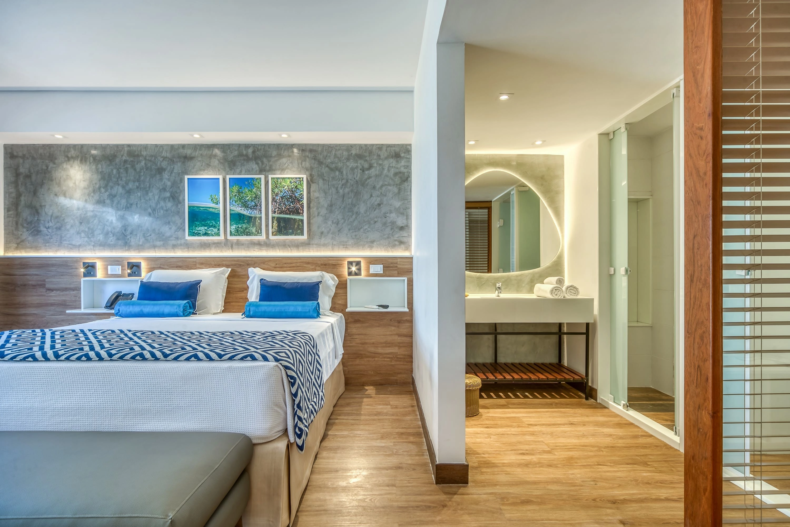 acomodações salinas maragogi Apartamento Standard Vitória-Régia, uma das acomodações do Salinas Maragogi, com cama uma queen size, banheiro e decoração aconchegante composta por madeira, luminárias e uma composição de quadros de praias de Maragogi.