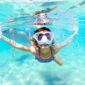 Mergulho nas Piscinas Naturais de Maceió Menina sorrindo com máscara de snorkel em um mergulho nas águas cristalinas e azul-turquesa das piscinas naturais de Maceió, em uma foto que mostra tanto o fundo do mar quanto o céu azul na superfície.