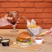 Hambúrguer no All Inclusive Dois hambúrgueres artesanais servidos com batatas fritas, molho e milkshake em mesa de tijolos à vista