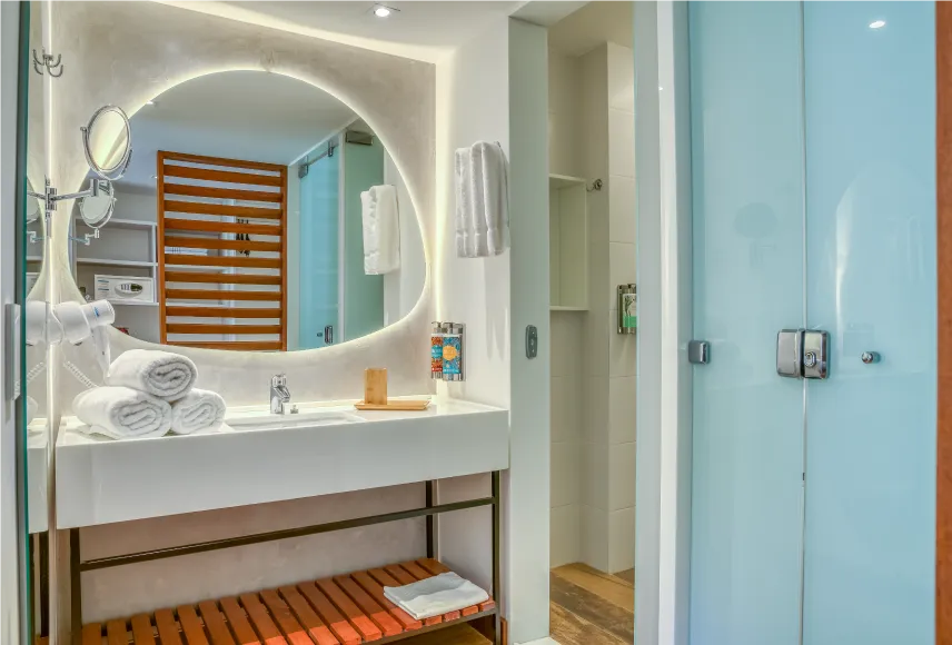 vitória-régia Banheiro do Standard Vitória-Régia, com espelho em formato orgânico acima da pia, toalhas dispostas em cima do balcão e pendurada ao lado da pia, espelho de aproximação, secadores, decoração e amenities L’Occitane.