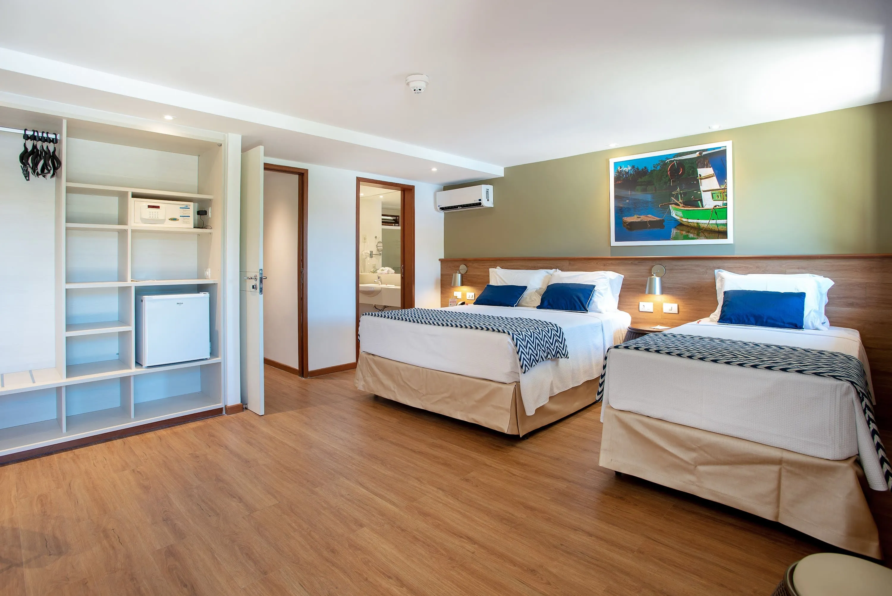 apartamento familiar maragogi Otra configuración de la Suite Familia, alojamiento en el Salinas Maragogi Resort Todo Incluido, con una cama queen size, una cama individual, armario, minibar, lámparas, decoración en madera, una imagen de una balsa en el río Maragogi y puerta al baño.