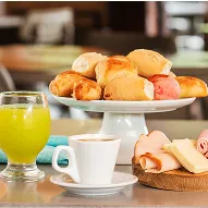 All Inclusive no café da manhã Mesa com pães, frios, queijos, café, sucos e bolo em ambiente de restaurante