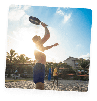 Hóspede jogando frescobol na praia sob o sol, aproveitando o dia de lazer no Salinas Maceió