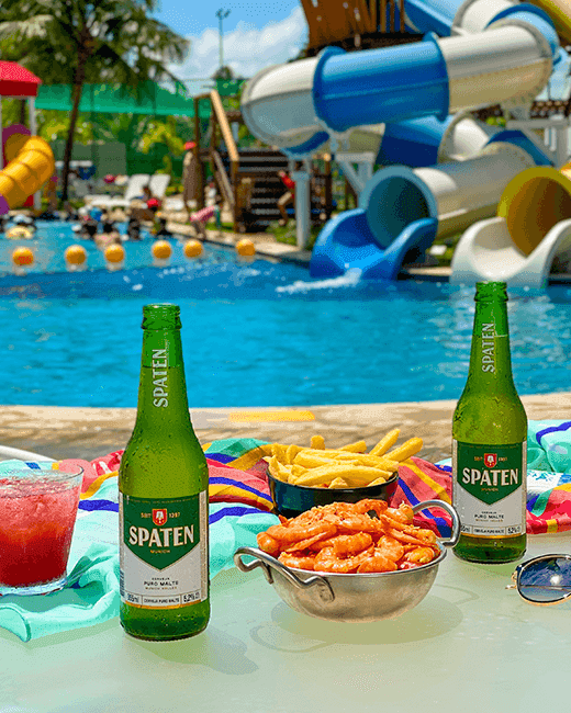 Mesa na beira da piscina infantil do Salinas Maragogi mostrando variedade de petiscos e drinks.