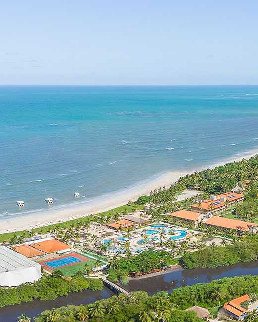 Vista aérea do Salinas Maragogi, com suas acomodações, complexos de piscinas e pontos de consumo, cortado pelo Rio Maragogi e localizado à beira-mar.