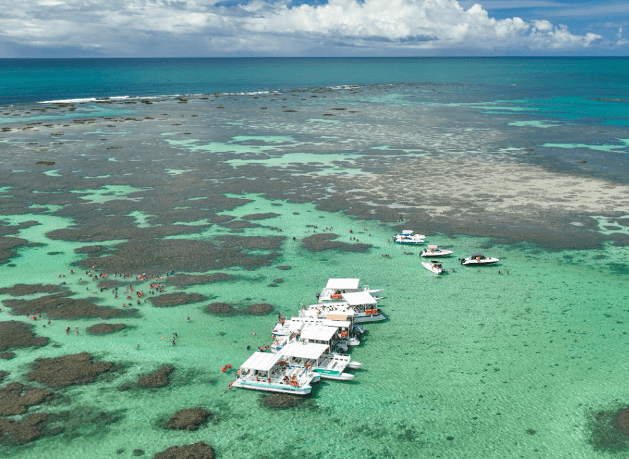 Vista aérea das Galés de Maragogi, com barcos e turistas aproveitando as piscinas naturais de águas cristalinas e recifes de corais