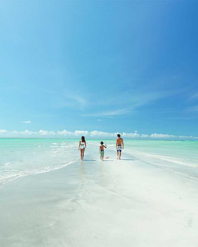 férias nordeste Fanília caminhando sobre faixa de areia branca que surge na maré baixa entre o mar azul turquesa da praia de Antunes, em Maragogi.