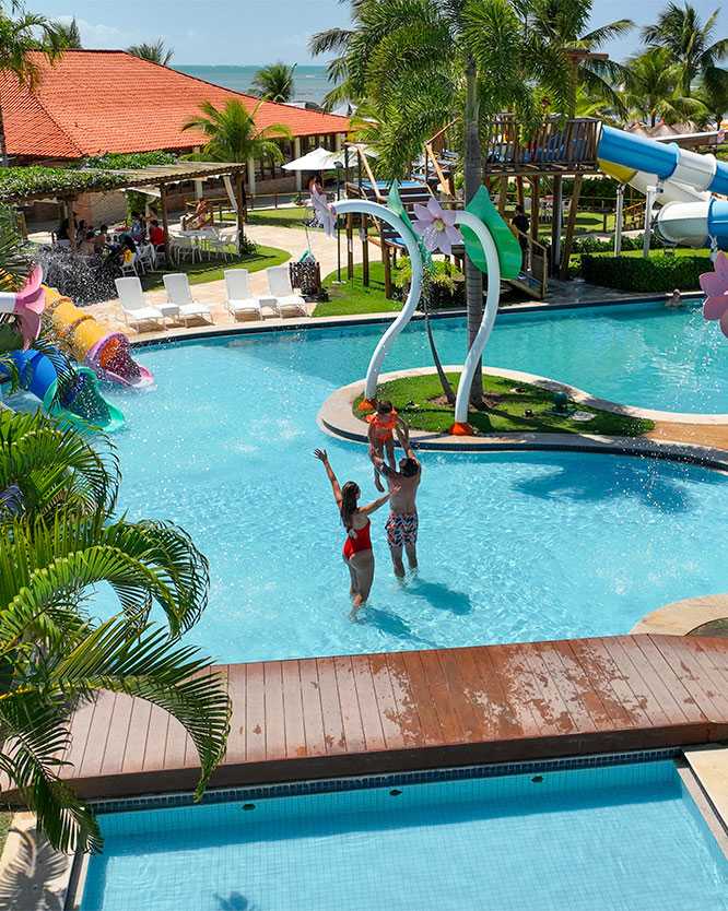 piscina infantil salinas maragogi Família na piscina infantil do Salinas Maragogi. O pai segura a filha nos braços e a mãe está de braços abertos dentro da piscina para crianças do resort.
