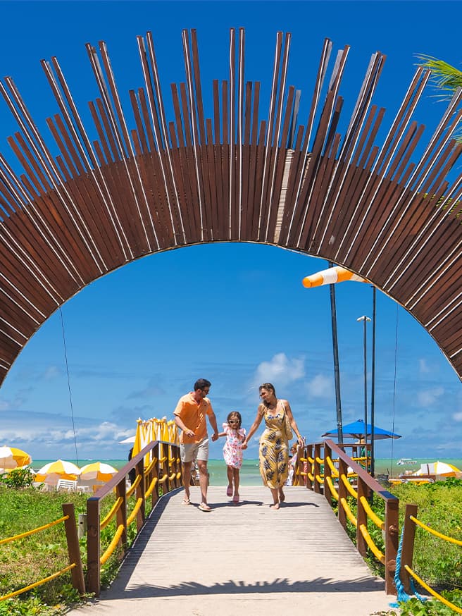 Onde as férias começam Portal do Salinas Maragogi cercado por coqueiros na beira do mar com céu azul.